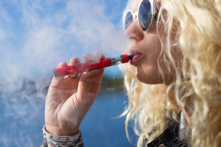 Frau inhaltiert Dampf aus einer E-Zigarette: Mediziner warnen vor schweren Folgen.
