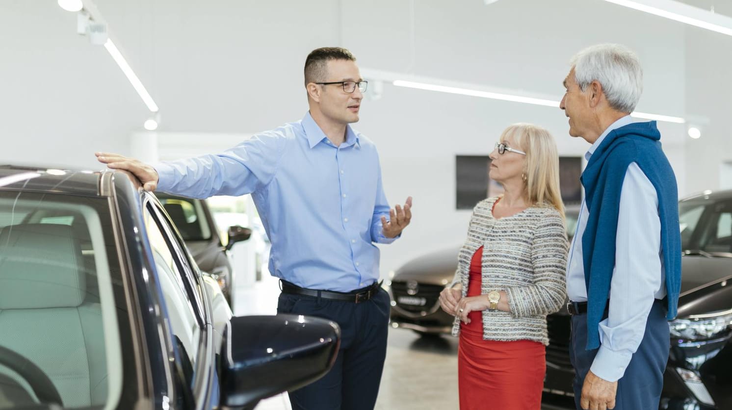 Älteres Ehepaar im Gespräch mit einem Autohändler: Verbraucher sollten Vertragsunterlagen vor dem Unterschreiben stets gründlich durchlesen.