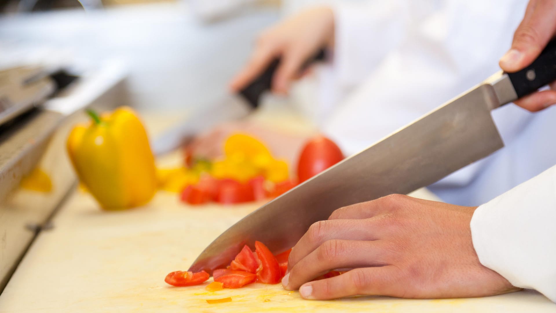 Koch schneidet Tomaten auf weißem Brett: Rotes Gemüse hinterlässt oft rote oder gelbe Flecken auf hellem Plastik.