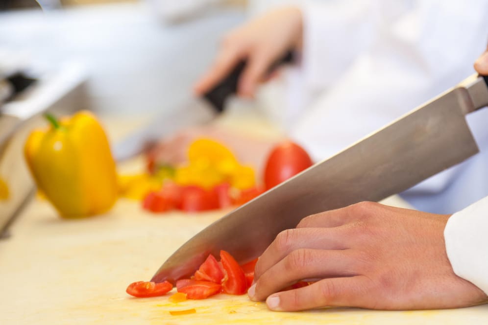Koch schneidet Tomaten auf weißem Brett: Rotes Gemüse hinterlässt oft rote oder gelbe Flecken auf hellem Plastik.