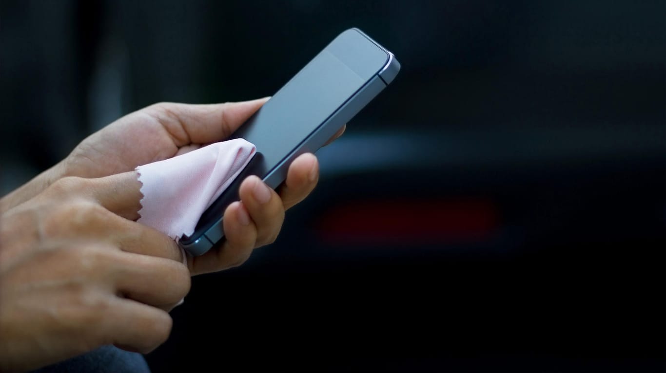 Eine Frau wischt das Smartphone-Display mit einem Tuch ab: Aus Hygienegründen sollte man das Handy von Zeit zu Zeit reinigen.