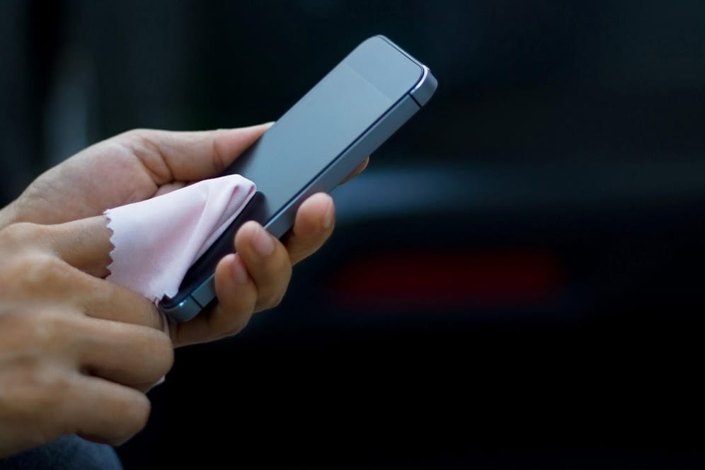 Eine Frau wischt das Smartphone-Display mit einem Tuch ab: Aus Hygienegründen sollte man das Handy von Zeit zu Zeit reinigen.