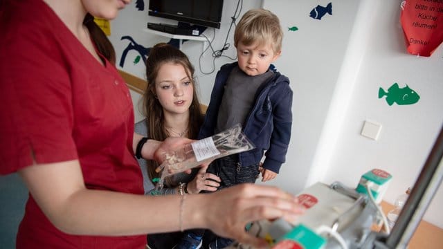 Levin Gebhardt sitzt auf Schoß seiner Mutter Lea, während eine Pflegerin eine Infusion vorbereitet.