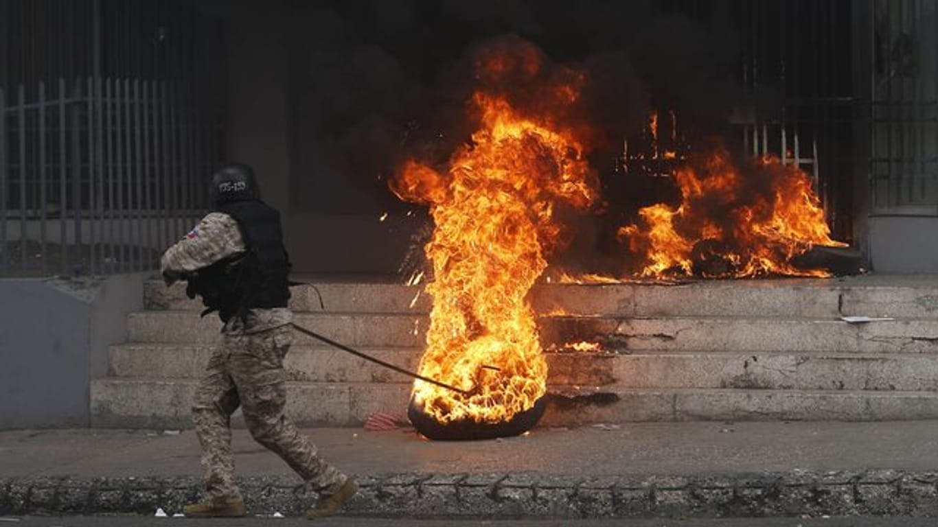 Ein Polizist entfernt einen brennenden Reifen vor einem Regierungsgebäude.