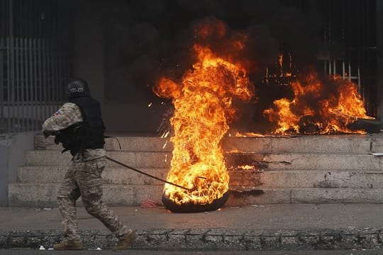 Ein Polizist entfernt einen brennenden Reifen vor einem Regierungsgebäude.