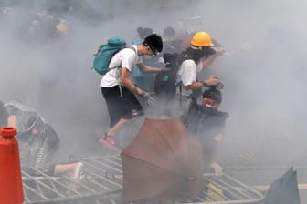 Hongkong: Demonstranten tragen in einer Tränengaswolke Gesichtsmasken und klettern über eine umgestürzte Absperrung.