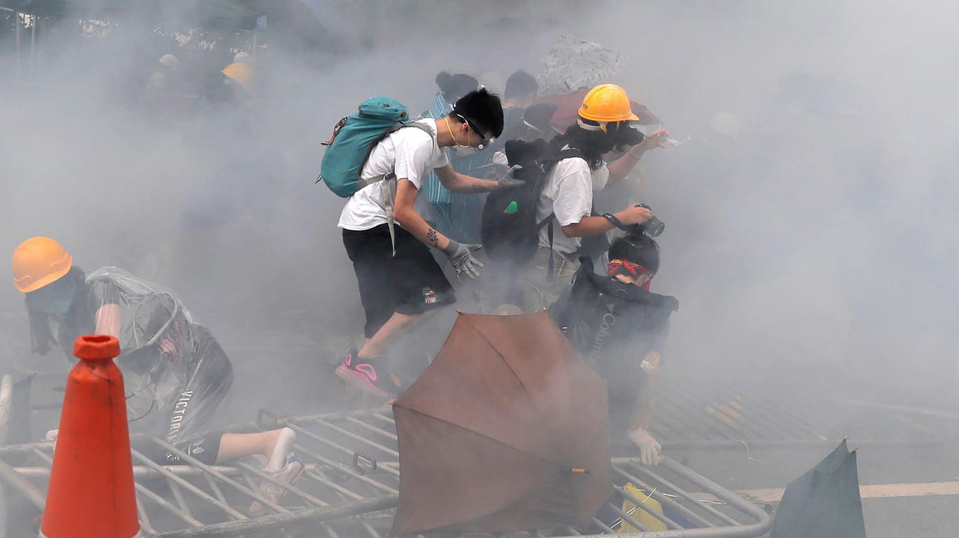 Hongkong: Demonstranten tragen in einer Tränengaswolke Gesichtsmasken und klettern über eine umgestürzte Absperrung.