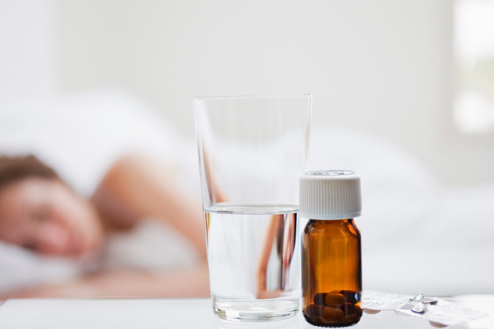 Frau schläft, auf dem Nachttisch liegen Medikamente: Wer Schlafstörungen hat oder glaubt, welche zu haben, greift oft zu Pillen.