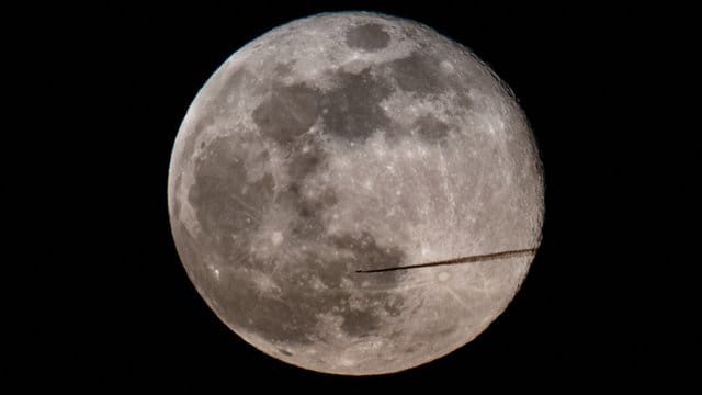 Ein Flugzeug fliegt am Abend am Vollmond vorbei.