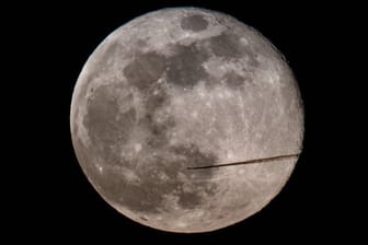 Ein Flugzeug fliegt am Abend am Vollmond vorbei.