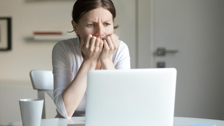 Eine Frau sitzt vor dem Notebook und hält sich die Hände vor den Mund: Auch Beleidigungen im Internet können den Betroffenen schwer zusetzen.
