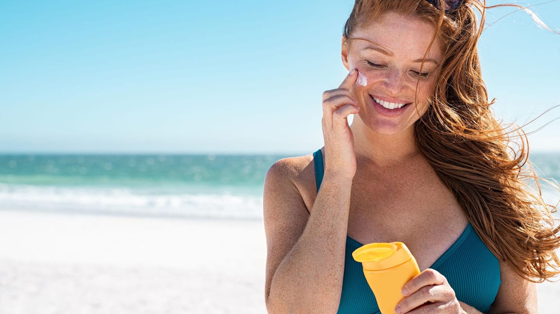 Woman with freckles applying sunscreen on face Woman with freckles applying sunscreen on face