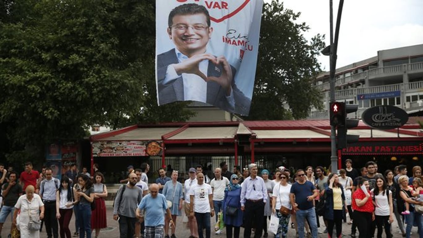 Menschen gehen unter einem Wahlplakat des Bürgermeisterkandidaten Imamoglu der Mitte-Links-Partei CHP entlang.