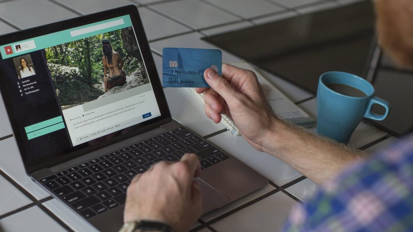 Ein Mann sitzt mit seiner Kreditkarte in der Hand vor einem Notebook: Zahlen Sie bei der Buchung einer Ferienunterkunft nicht sofort den Gesamtbetrag.