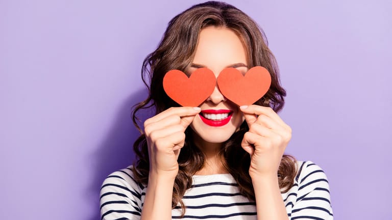 Eine Frau hält zwei Herzen vor ihre Augen: Mit der rosaroten Brille können Verliebte ihr Gegenüber schwerer einschätzen. (Symbolbild)