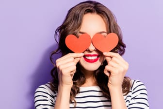 Eine Frau hält zwei Herzen vor ihre Augen: Mit der rosaroten Brille können Verliebte ihr Gegenüber schwerer einschätzen. (Symbolbild)