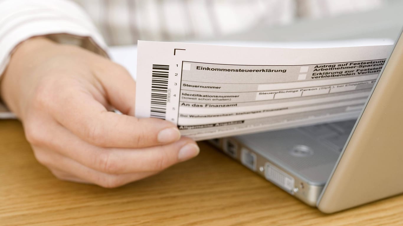 Hand hält ein Dokument für die Einkommenssteuererklärung über einem Laptop: Sie können Ihr Notebook und Ihr Smartphone teilweise von der Steuer absetzen.