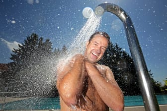 Mann beim Duschen im Freibad: Kaltes Wasser von außen kann die Körpertemperatur erst einmal herunterregeln.