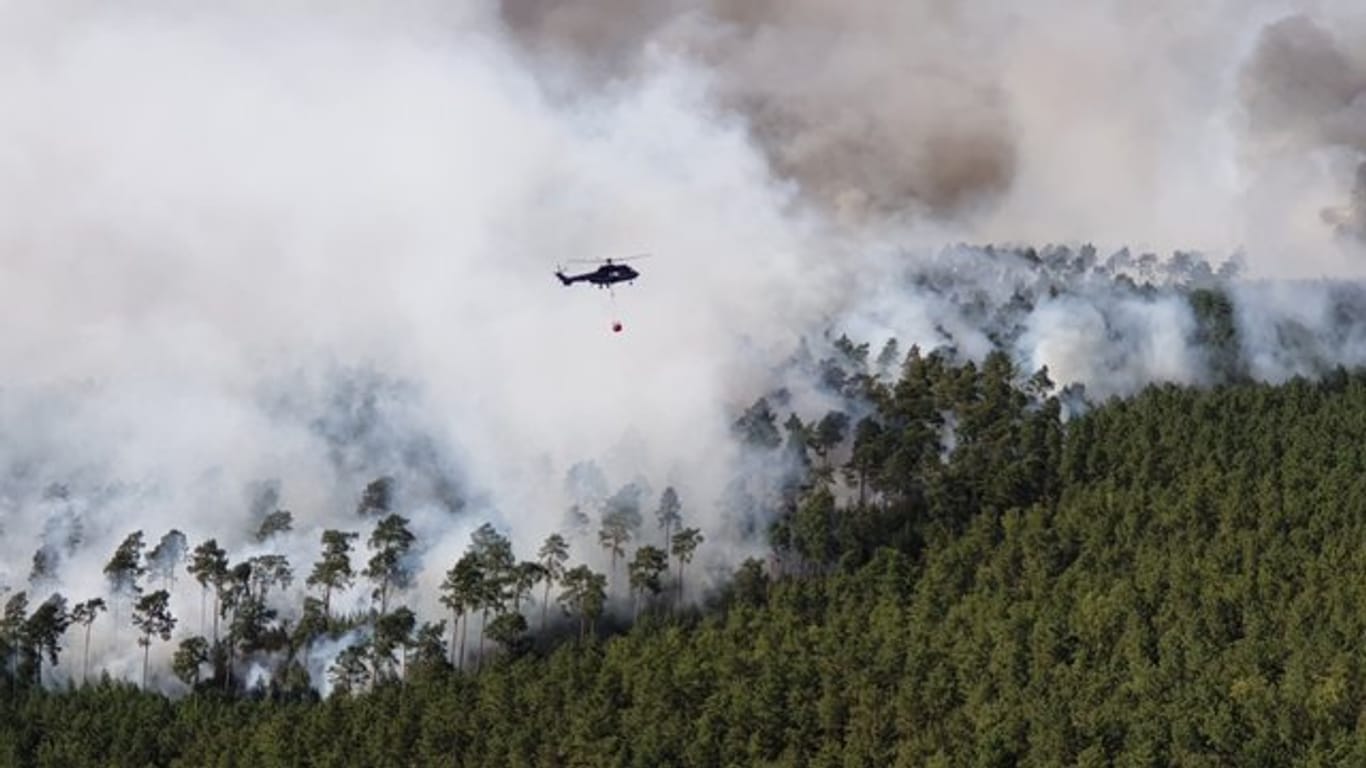 Ein Hubschrauber der Bundespolizei fliegt bei Löscharbeiten über einem Waldstück in der Lieberoser Heide.