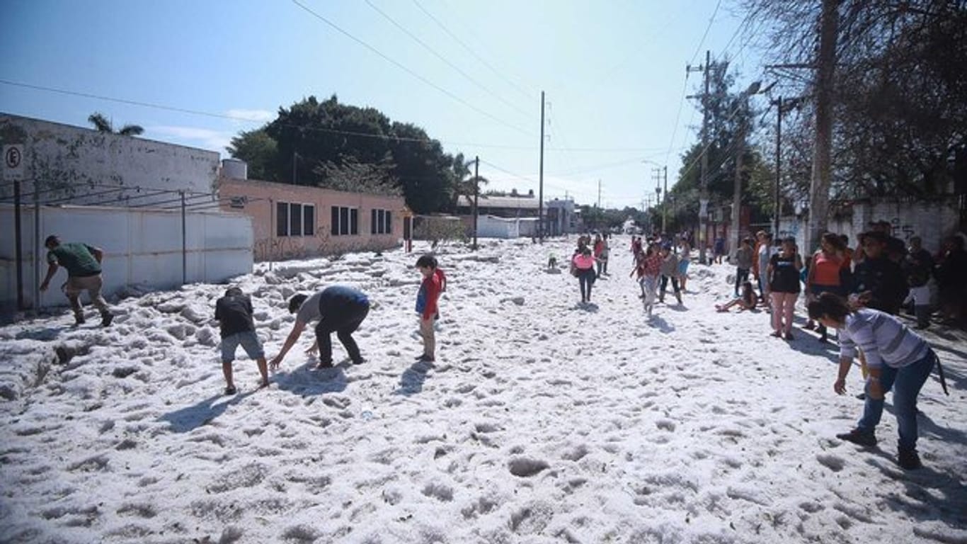 Kinder begutachten die dicke Hagelschicht auf einer Straße in der Stadt Guadalajara.