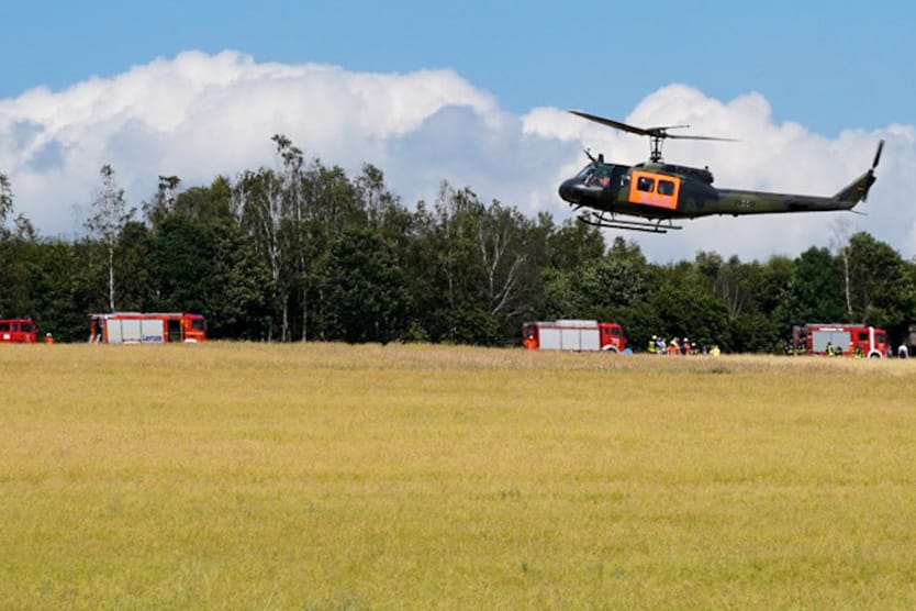 Unglücksstelle in Niedersachsen: Ein Hubschrauber der Bundeswehr landet auf einer Wiese während im Hintergrund Feuerwehrfahrzeuge stehen.