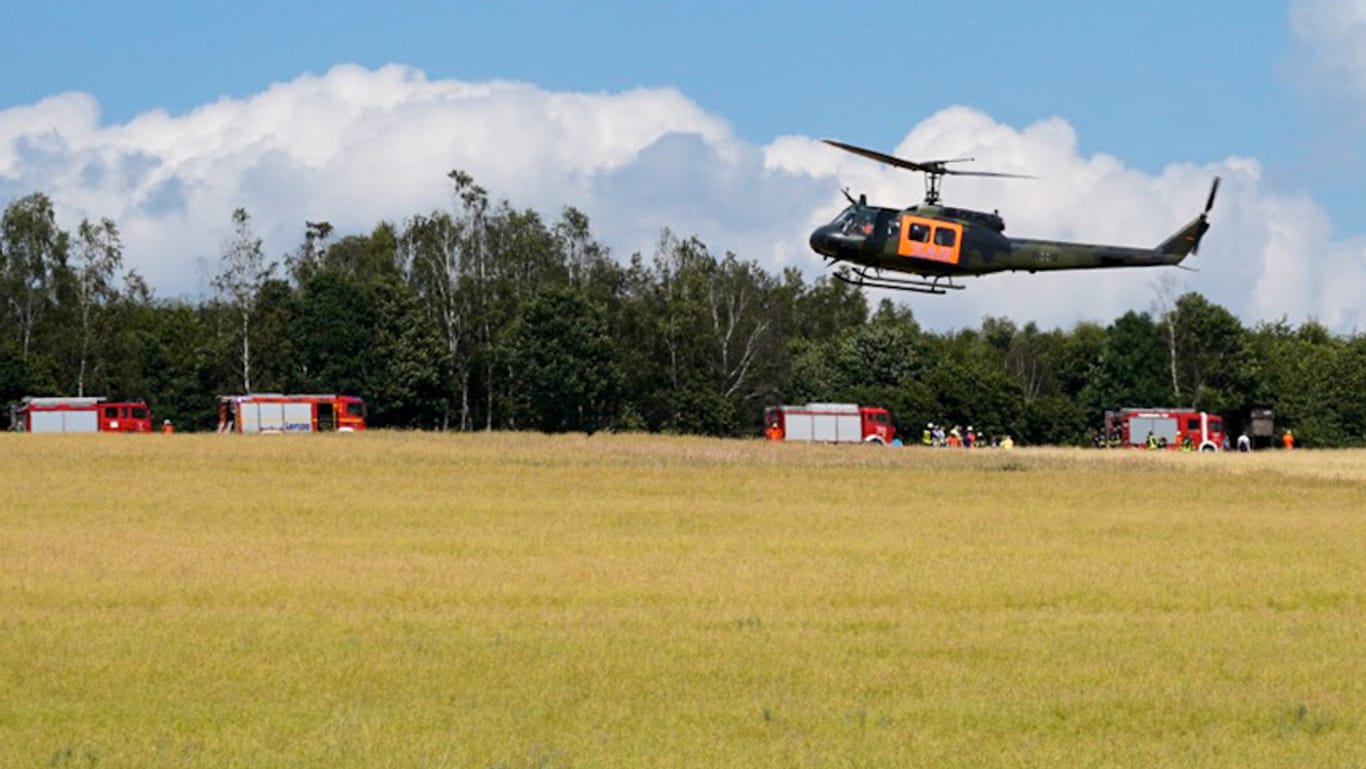Unglücksstelle in Niedersachsen: Ein Hubschrauber der Bundeswehr landet auf einer Wiese während im Hintergrund Feuerwehrfahrzeuge stehen.