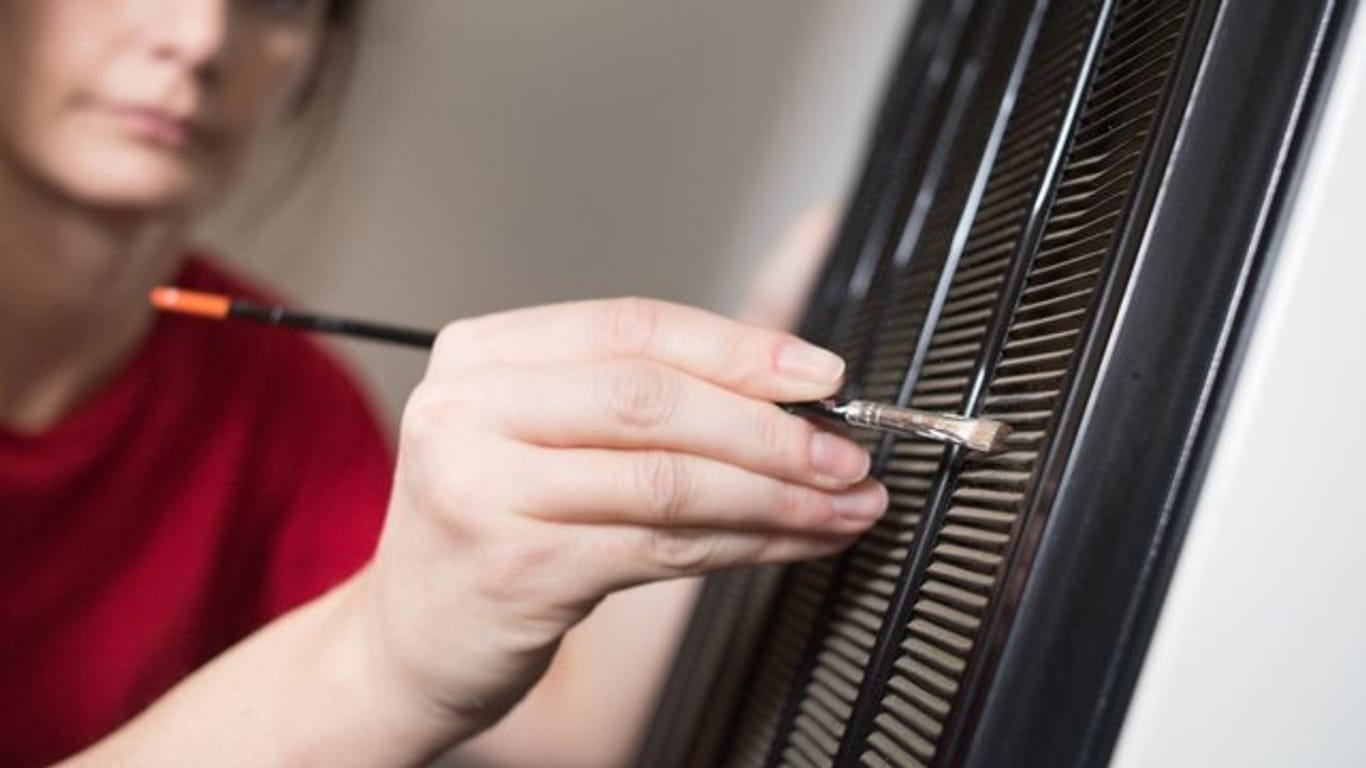 Eine Frau reinigt mit einem Pinsel die Lüftungsgitter: Reinigen Sie das Lüftungsgitter an der Rückseite, damit der Kühlschrank weniger Strom verbraucht.