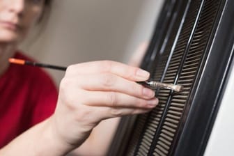 Eine Frau reinigt mit einem Pinsel die Lüftungsgitter: Reinigen Sie das Lüftungsgitter an der Rückseite, damit der Kühlschrank weniger Strom verbraucht.
