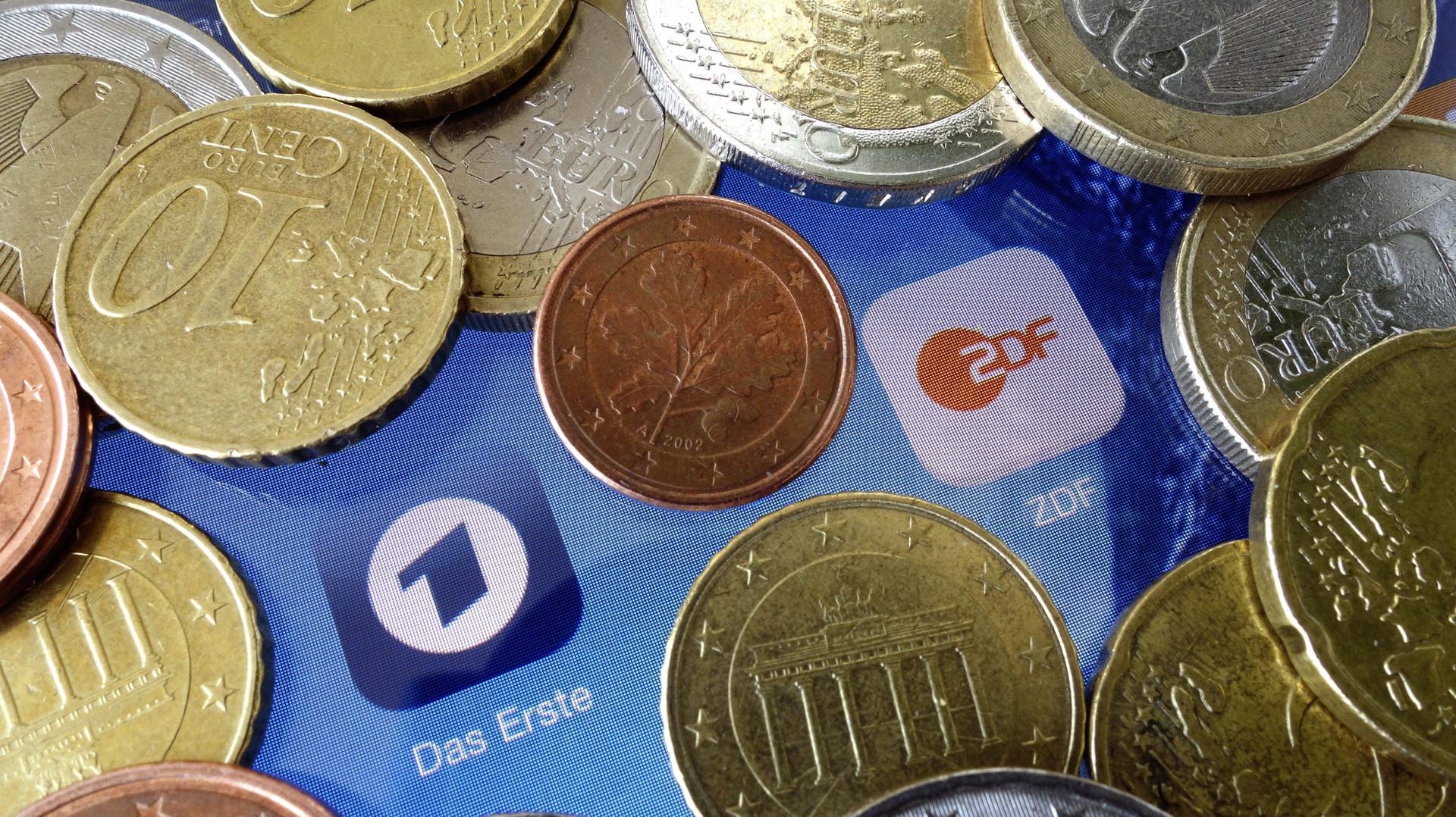 Euromünzen liegen neben den Logos der Apps von ARD und ZDF: Die Erträge aus dem Rundfunkbeitrag sind im vergangenen Jahr ganz leicht gestiegen.