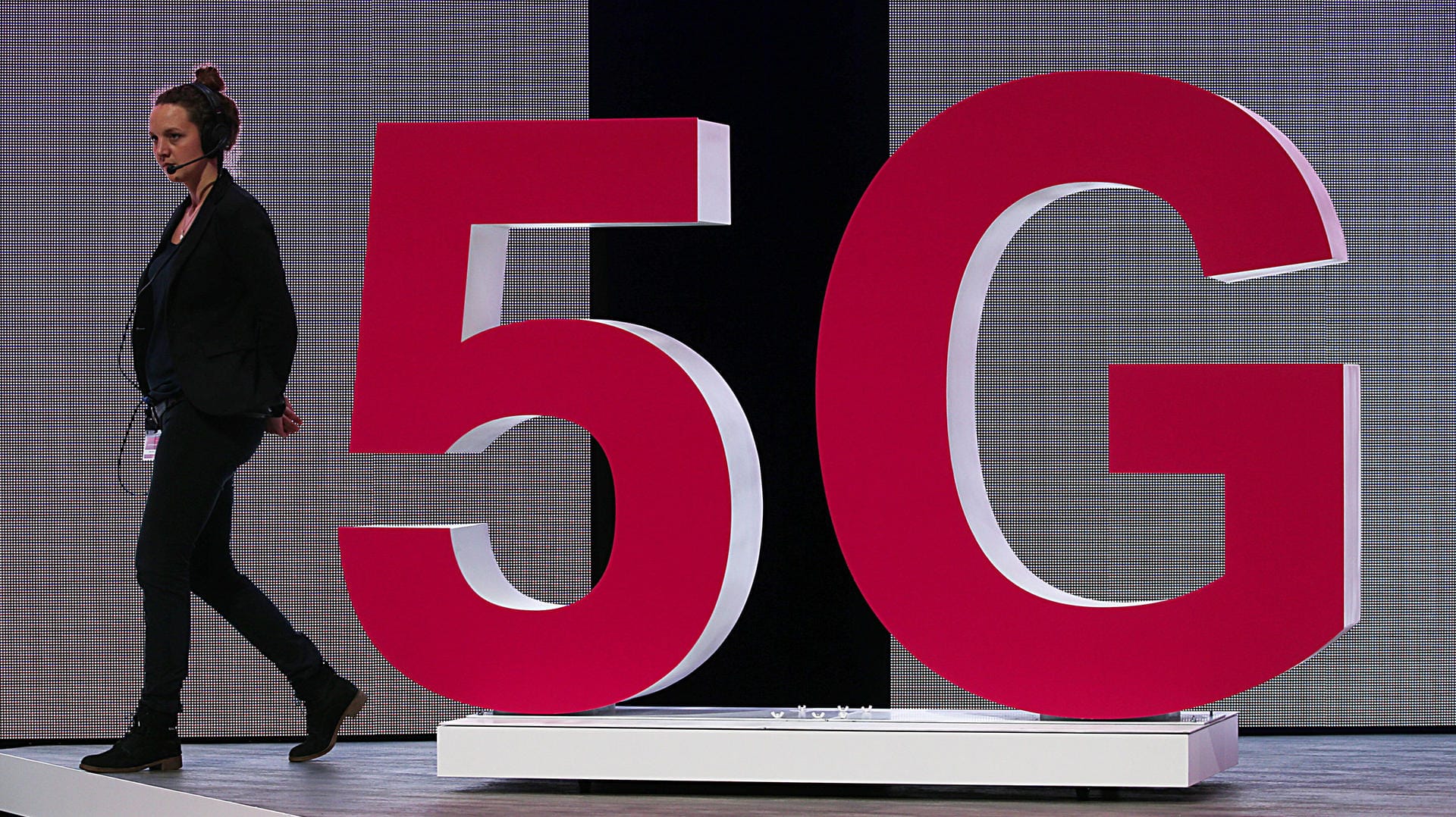 Eine Mitarbeiterin der Telekom geht an einem 5G Logo vorbei: Die Deutsche Telekom hat drei Wochen nach der Versteigerung der Frequenzen für die fünfte Mobilfunkgeneration sein 5G-Netz für Kunden geöffnet.