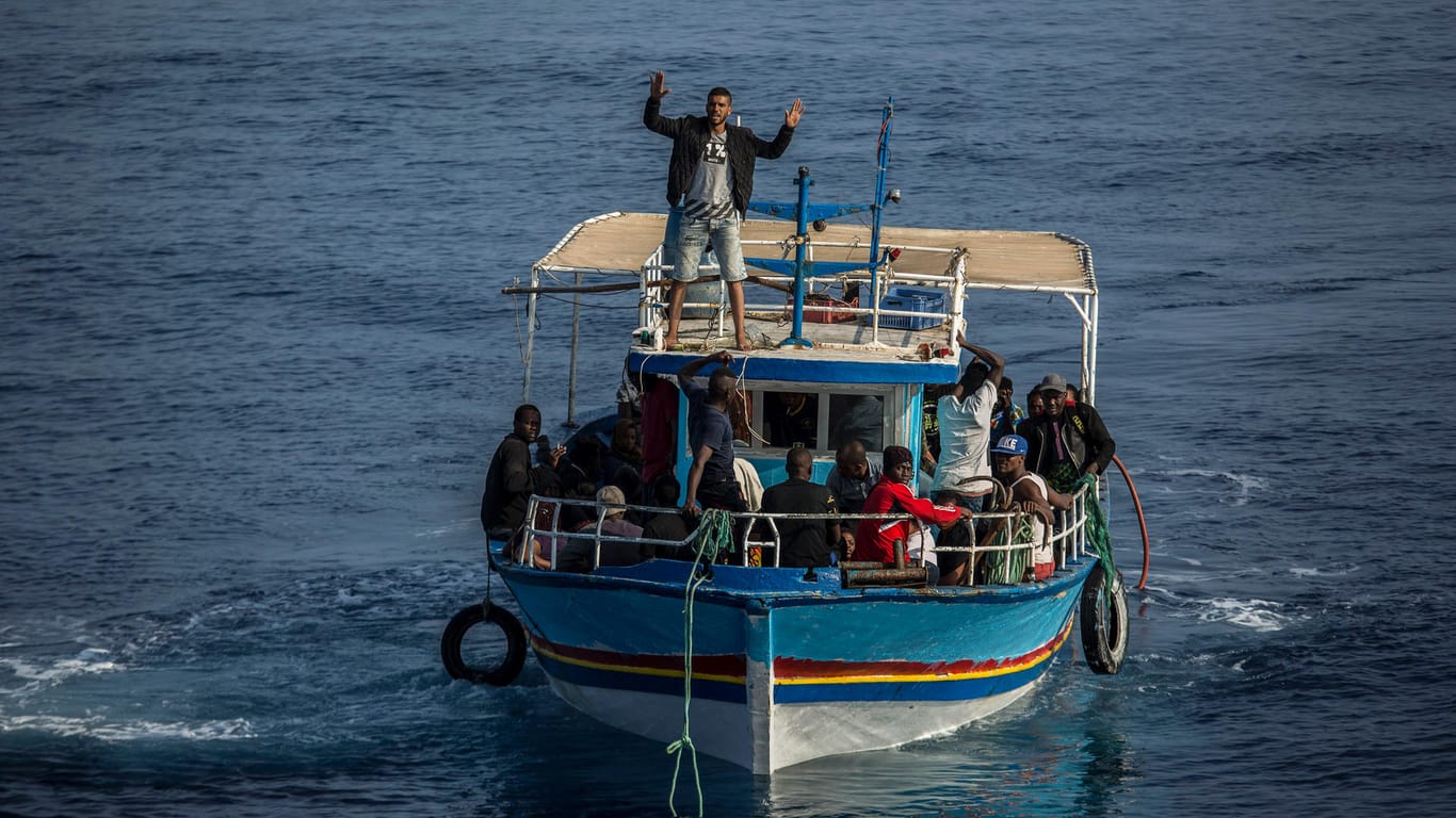 Ein Migrant an Bord eines Bootes winkt in Richtung des Rettungsschiffs Open Arms der spanischen Organisation Proactiva Open Arms (Symbolbild): Immer wieder verunglücken Schiffe wie dieses auf der Überquerung des Mittelmeers.