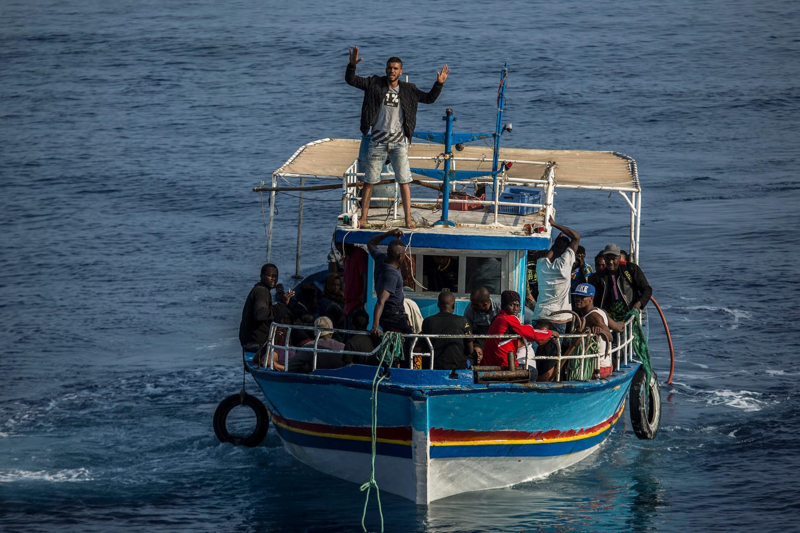 Ein Migrant an Bord eines Bootes winkt in Richtung des Rettungsschiffs Open Arms der spanischen Organisation Proactiva Open Arms (Symbolbild): Immer wieder verunglücken Schiffe wie dieses auf der Überquerung des Mittelmeers.