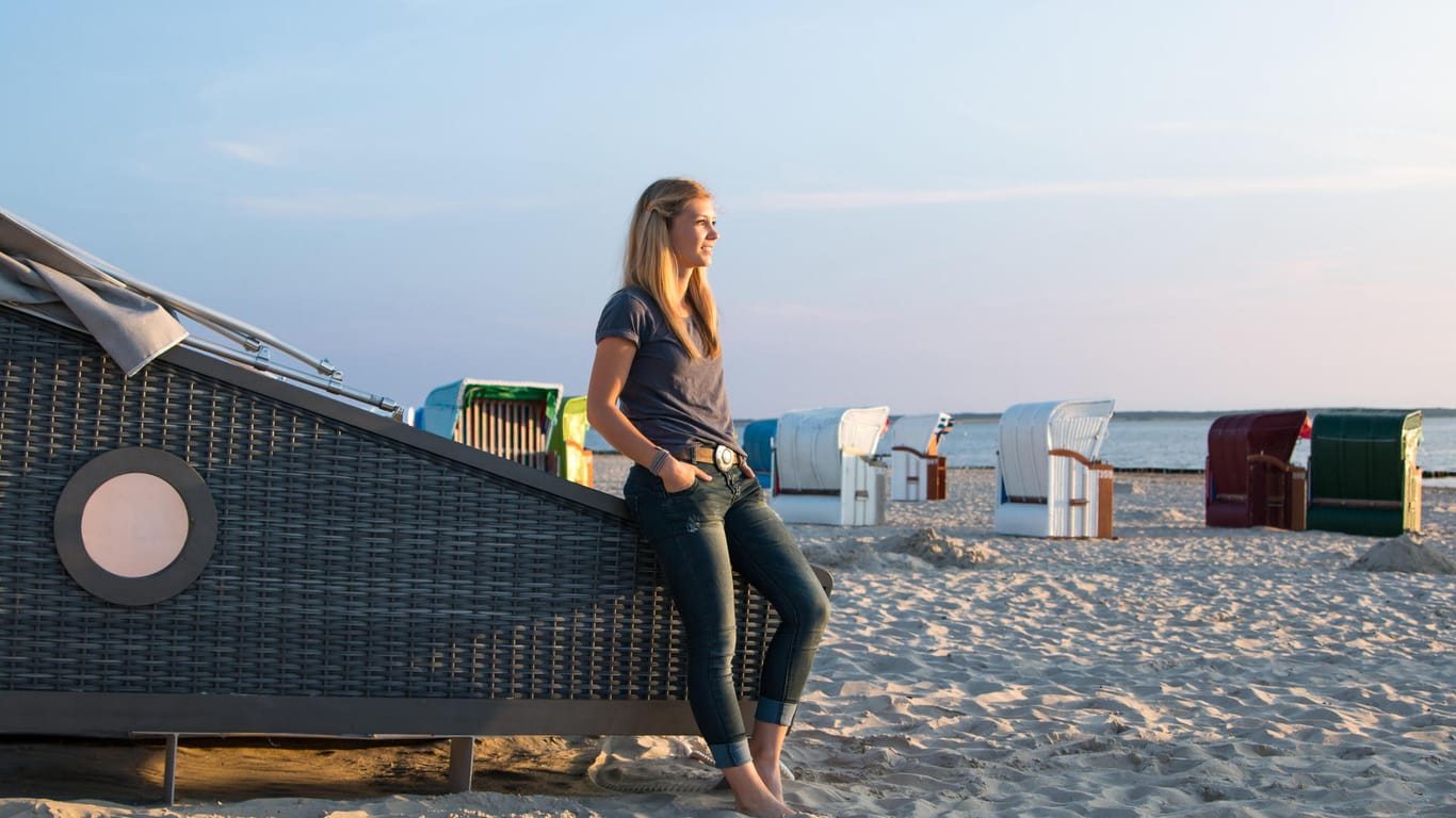 Frau steht an Strandschlafkorb: Auf der Nordseeinsel Föhr können Sie an fünf Standorten in speziellen Strandkörben übernachten.