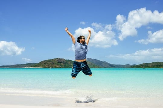 Mann springt am Strand in die Luft: Für ungetrübte Urlaubsfreude lohnt es sich, die rechtlichen Regelungen genau zu kennen. (Symbolbild)