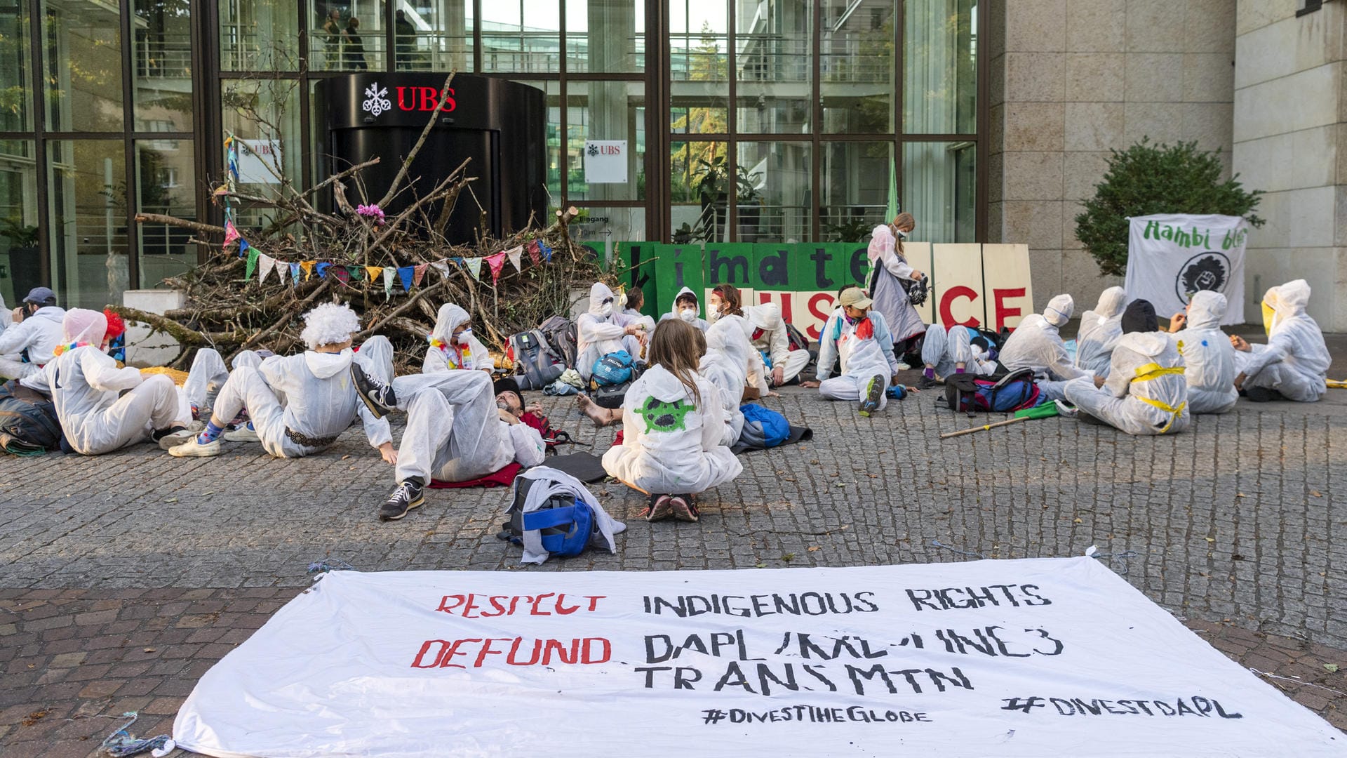 Basel: Aktivisten der Gruppe "Collective Climate Justice" blockieren mit Ästen den Eingang von dem UBS-Hauptsitz am Aeschenplatz und setzen beziehungsweise legen sich vor das Gebäude.