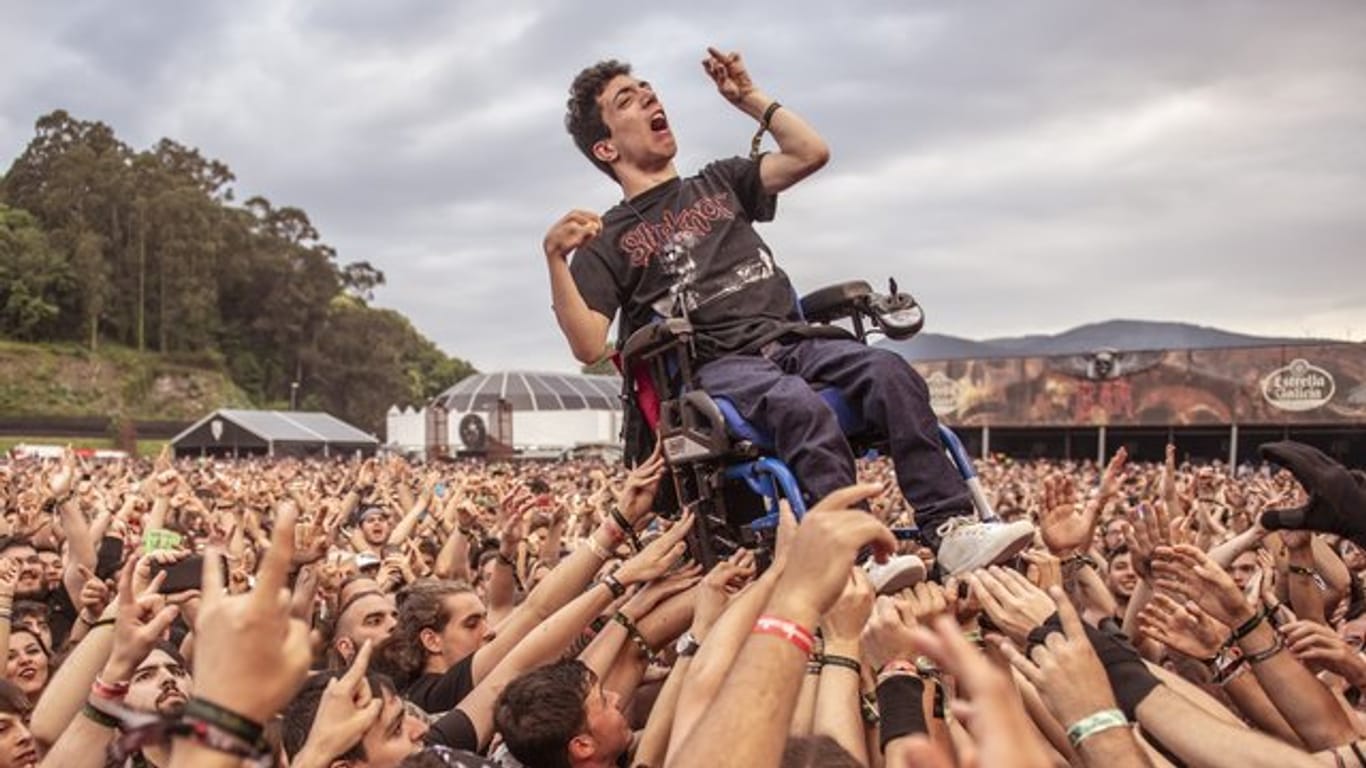 Ein junger Mann im Rollstuhl wird während des Konzertes von Arch Enemy beim "Resurrection Fest" in die Höhe gehoben.