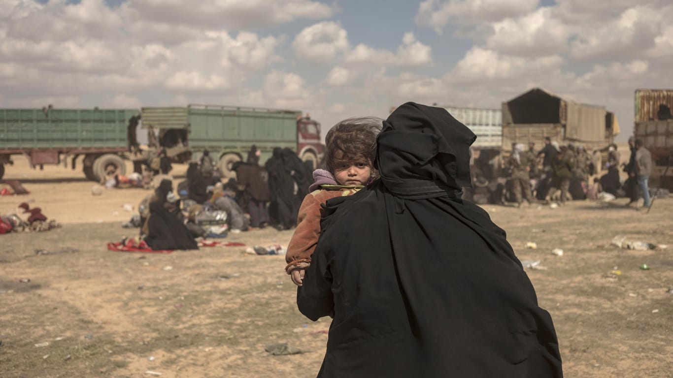 Eine Frau trägt ihr Kind durch ein Lager im syrischen Baghus