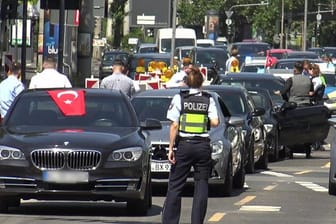 Eine Polizistin steht vor den Fahrzeugen eines türkischen Hochzeutskorsos.