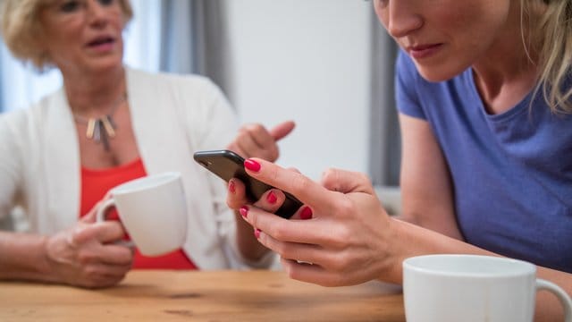 Frau mit Handy in der Hand: Wer gute Kommunikation pflegen will, sollte in einem ersten Schritt möglichst wertfrei beschreiben, was er im Moment wahrnimmt.