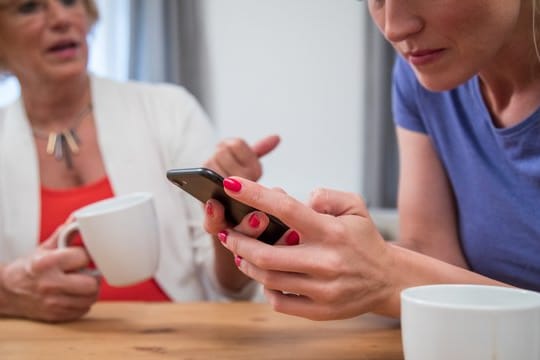 Frau mit Handy in der Hand: Wer gute Kommunikation pflegen will, sollte in einem ersten Schritt möglichst wertfrei beschreiben, was er im Moment wahrnimmt.