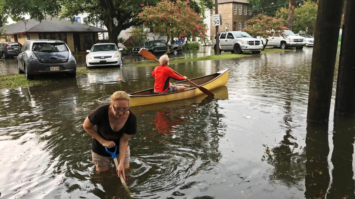 In Broadmoor, einem Teil von New Orleans, ist das Hochwasser angekommen: Eine Frau stochert mit einer Schaufel im Wasser, ein Mann fährt mit einem Kanu durch die Straße.