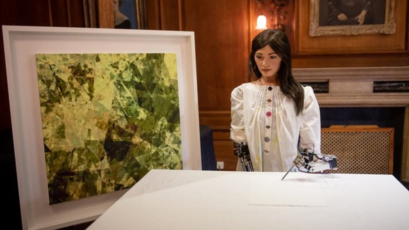 Ai-Da, die weltweit erste Roboterkünstlerin, in Oxford neben einem eigenen Kunstwerk.