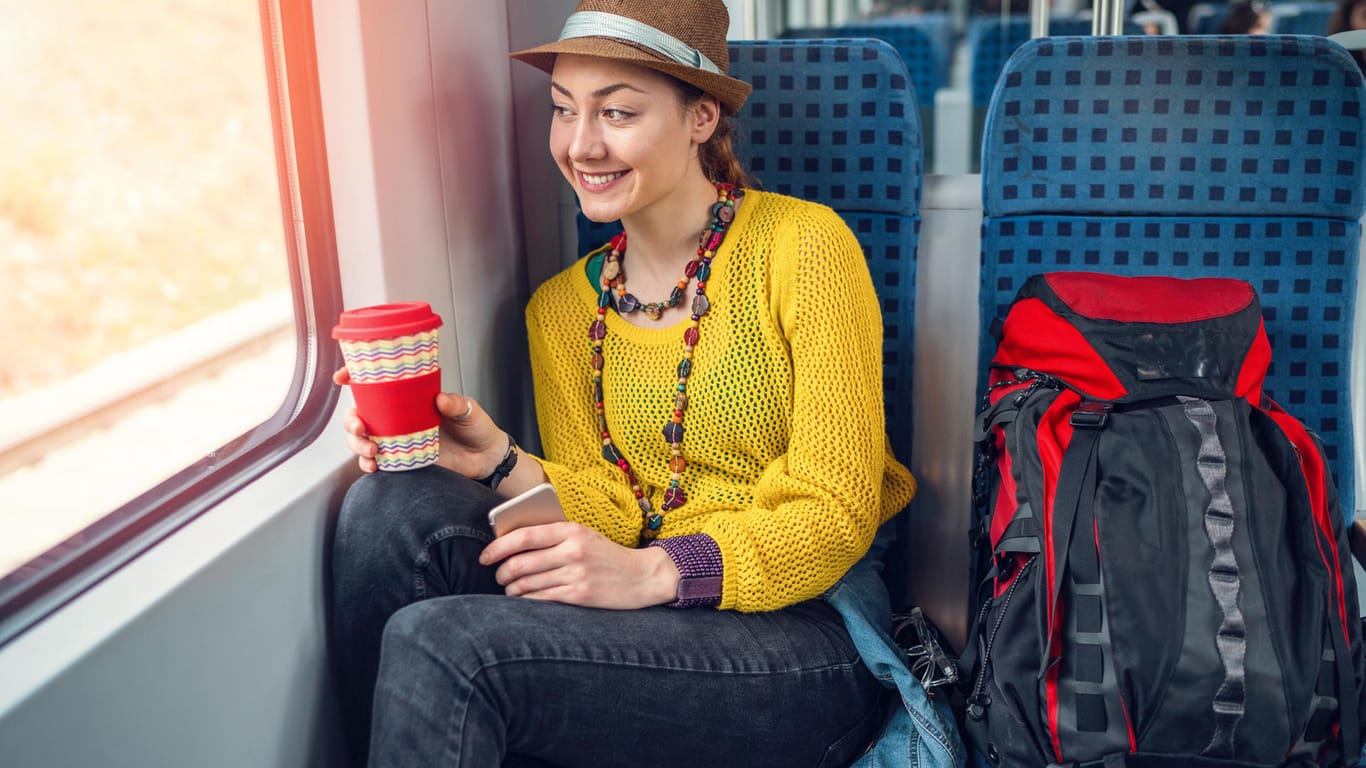 Frau sitzt mit einem Kaffee im Zug: Speisen und Getränke, die zu stark riechen, können andere Fahrgäste belästigen.