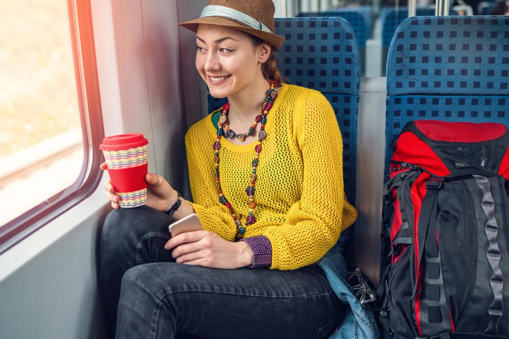 Frau sitzt mit einem Kaffee im Zug: Speisen und Getränke, die zu stark riechen, können andere Fahrgäste belästigen.