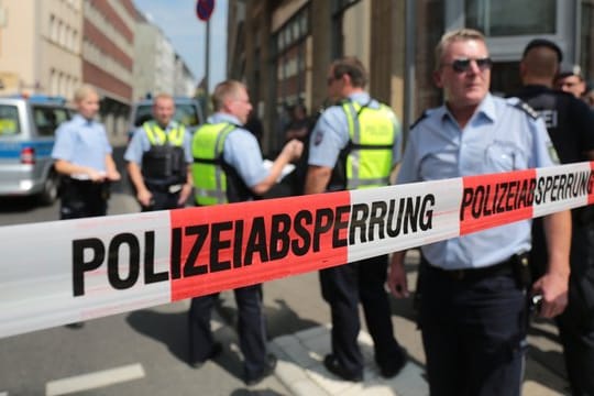 Polizisten stehen vor einem Wohngebäude eines der mutmaßlichen Gefährder in der Kölner Innenstadt hinter einem Absperrband.