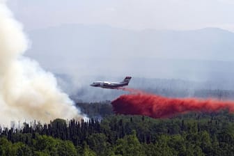 Ein Löschflugzeug lässt über einem in der Nähe von Montana Creek brennenden Wald Löschmittel ab.