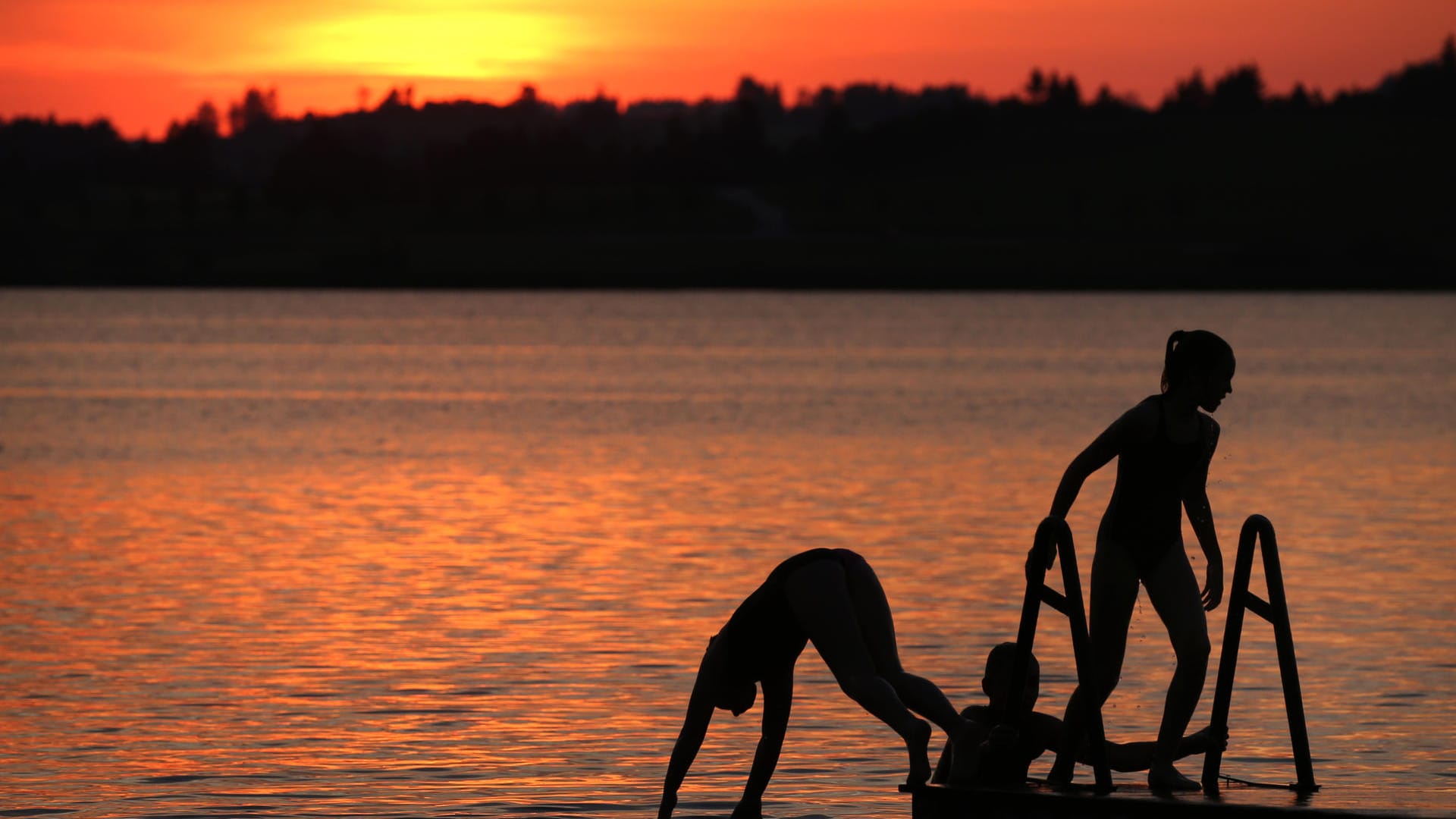 Bayern, Füssen: Urlauber springen während des Sonnenunterganges von einem Steg in den Hopfensee.