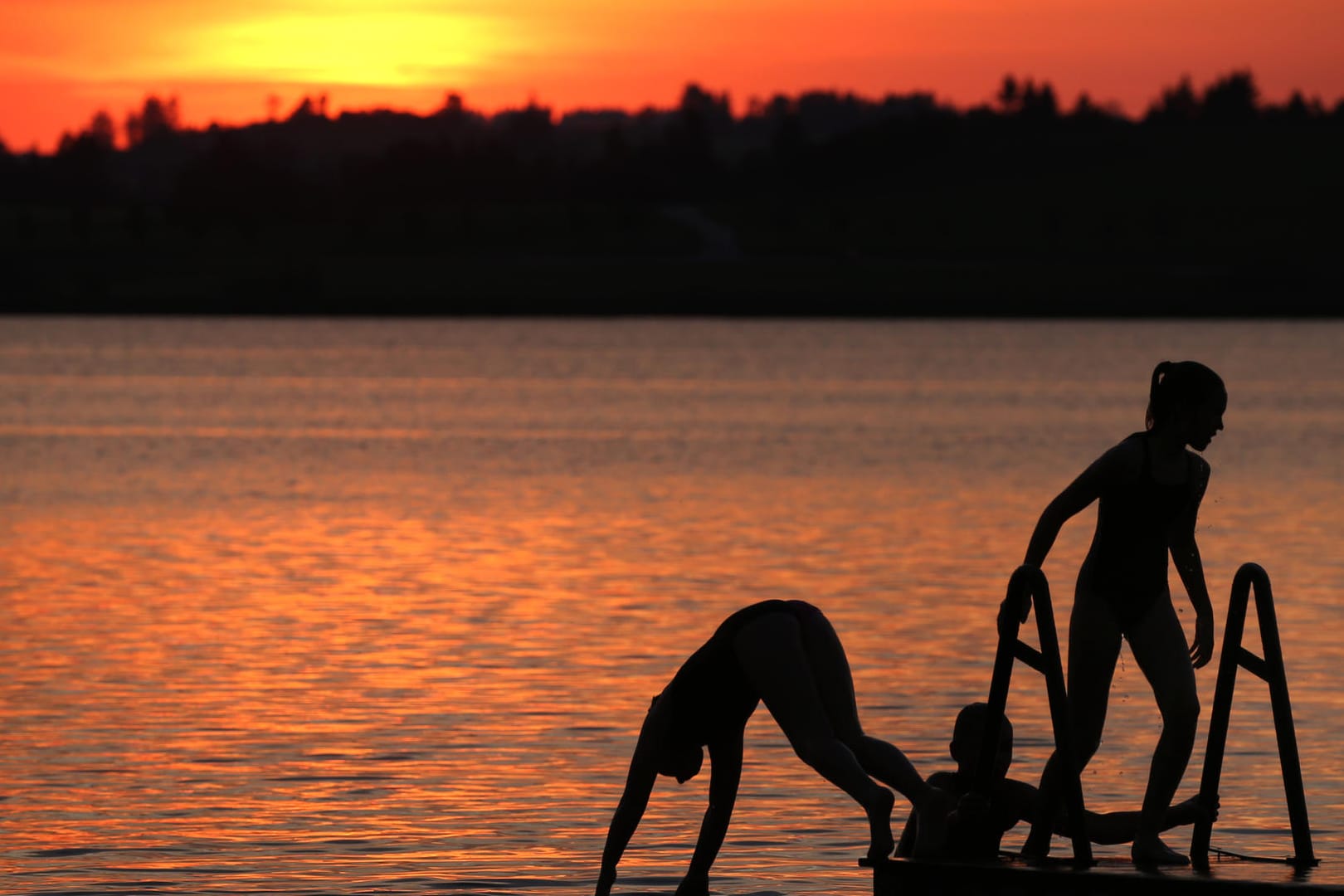 Bayern, Füssen: Urlauber springen während des Sonnenunterganges von einem Steg in den Hopfensee.