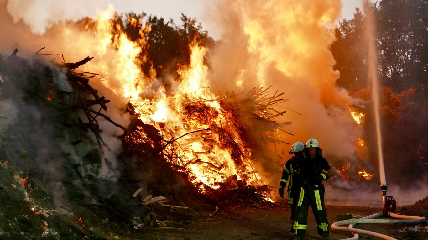 Feuerwehrleute stehen vor dem brennenden Grünabfallhaufen in Bochum: Seit den frühen Morgenstunden steht er in einer städtischen Kompostieranlage in Flammen.