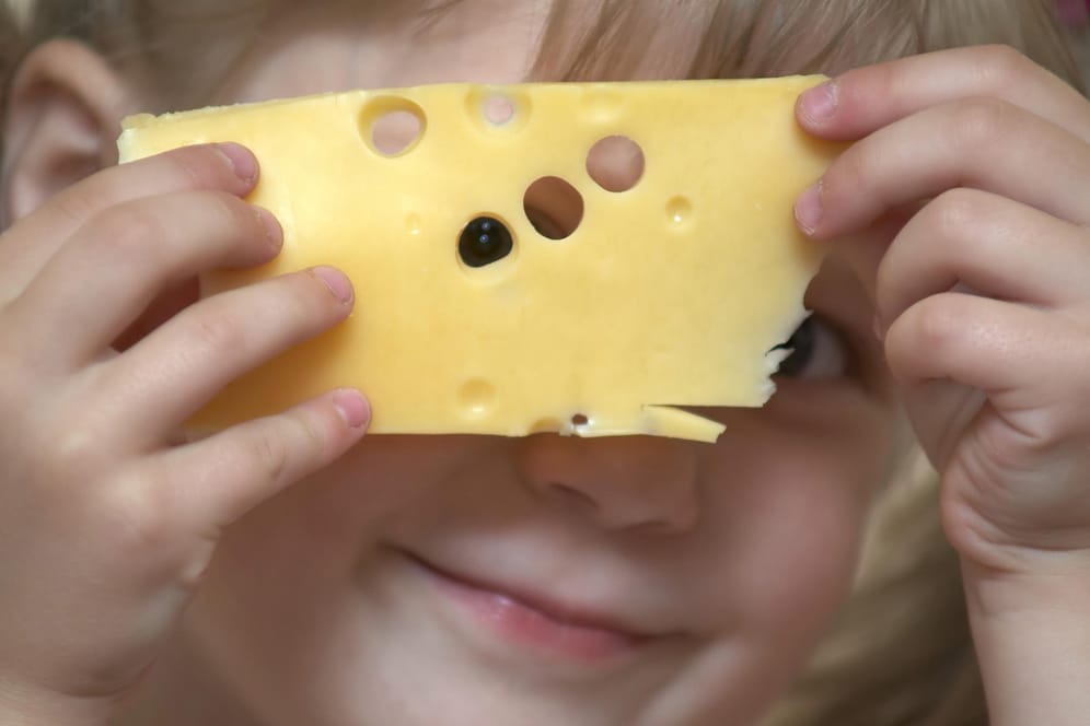 Ein Mädchen schaut durch die Löcher einer Käsescheibe: Musik kann den Geschmack von Milchprodukten beeinflussen.